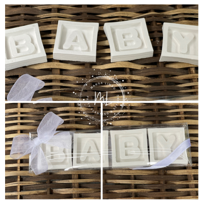 Blocos de letras brancos formando a palavra BABY sobre vime, alguns embalados com fita e laço branco