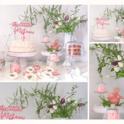 Mesa decorada com bolo de aniversário branco e flores, doces rosados e vasos com flores naturais.