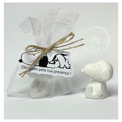 Figura decorativa de Snoopy em cerâmica branca ao lado de saco de tule com laço e etiqueta