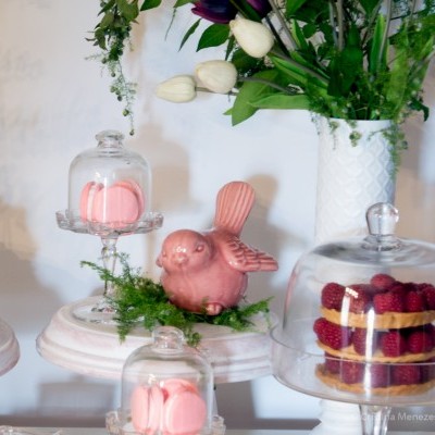 Suportes de vidro com macarons e sobremesa, vaso branco com flores e decoração de pássaro rosa