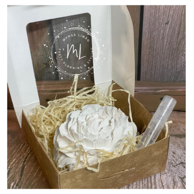 Caixa com flor decorativa branca, palha e frasco transparente, texto MANGA LIMÃO PARTY PLANNING & EVENTS na tampa