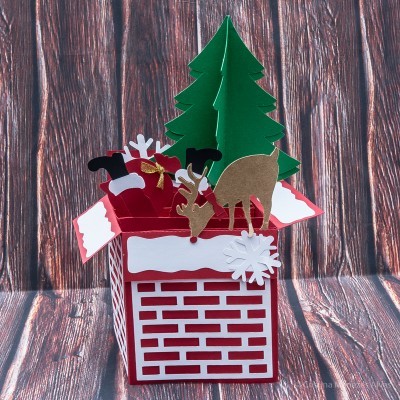 Caixa decorativa de Natal em papel com figuras tridimensionais sobre fundo de madeira.