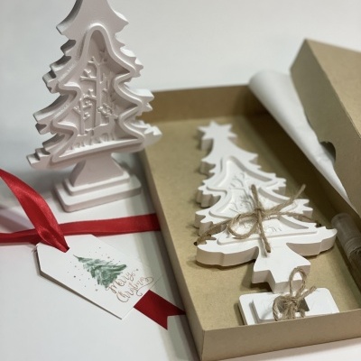 Árvores de Natal decorativas em madeira branca com etiqueta e fita vermelha.