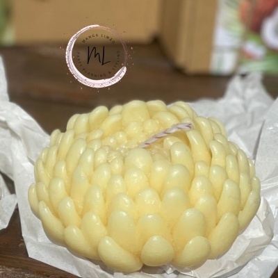 Vela amarela em forma de flor sobre papel branco e fundo de madeira com selo redondo à esquerda