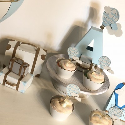 Cupcakes com toppers de balões e nuvens em exposição decorativa azul e branca