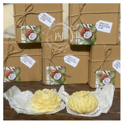 Caixas de cartão castanho com etiquetas e ilustração de cocos, duas velas em forma de flor em papel branco sobre mesa de madeira.