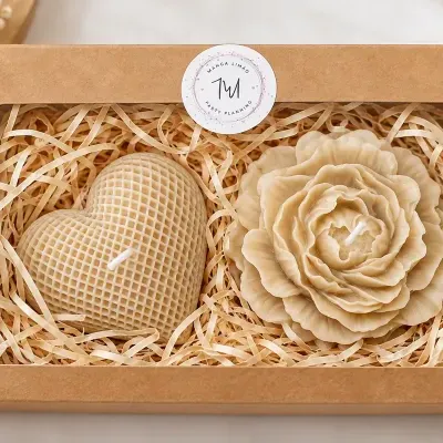 Caixa com duas velas bege, coração texturizado e flor detalhada, em caixa de cartão com janela transparente