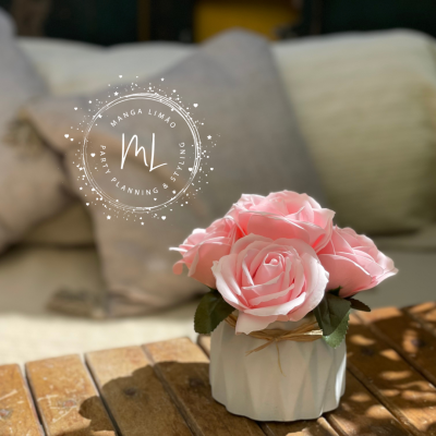 Vaso branco com flores cor de rosa sobre mesa de madeira e almofadas ao fundo