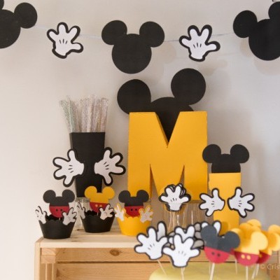 Decoração temática Minnie e Mickey Mouse com silhuetas, luvas e letras amarelas sobre mesa de madeira