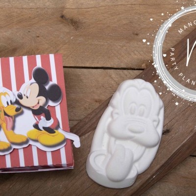 Borracha branca em forma do Pateta ao lado de caixa decorativa com Mickey e Pluto sobre madeira clara