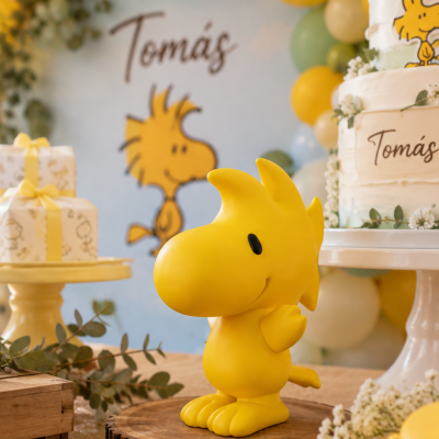 Figura de Woodstock amarela em festa decorada com balões e bolo com texto Tomás