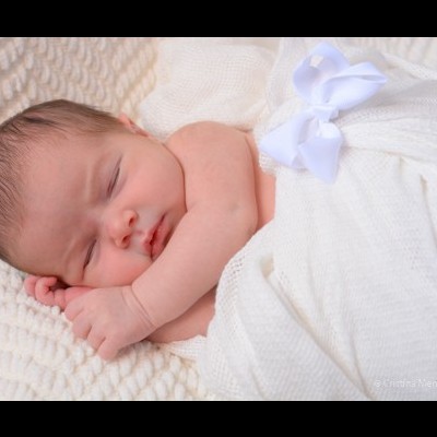Bebé recém-nascido a dormir embrulhado em manta branca com laço