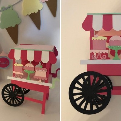 Carrinho decorativo rosa e vermelho com roda preta grande e bolos em miniatura