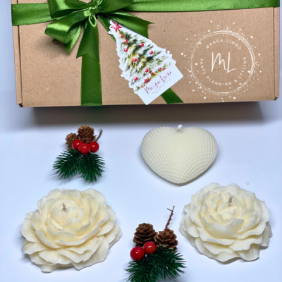 Conjunto de velas decorativas brancas em forma de flores e coração com adornos de pinhas e frutos vermelhos ao lado de caixa castanha com laço verde
