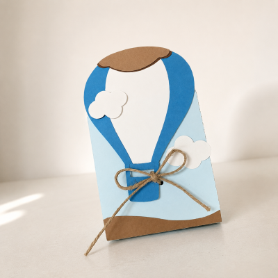 Cartão decorativo de balão de ar quente em cartão azul, branco e castanho com laço de corda.