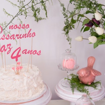 Bolo branco com decoração de topo cor-de-rosa e flores brancas e roxas num arranjo