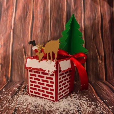 Caixa decorativa natalícia com rena, árvore e laço vermelho sobre fundo de madeira