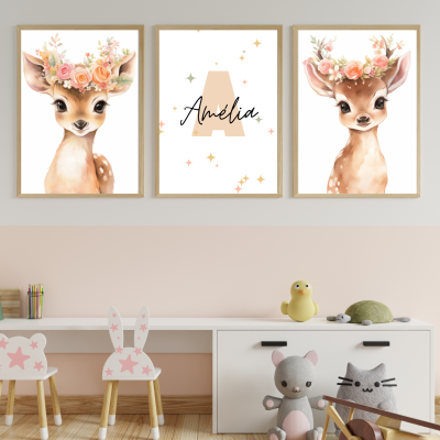 Três quadros com veados e nome Amélia pendurados numa parede sobre mobília branca com brinquedos e cadeiras pequenas.