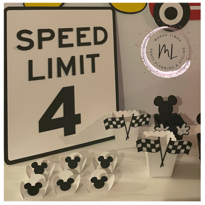 Placa de velocidade com texto e suportes para doces com figura de Mickey Mouse e bandeiras quadriculadas.