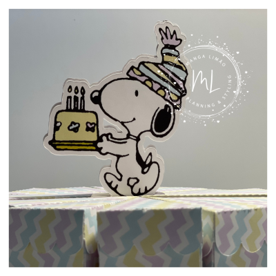 Figura de Snoopy com bolo e chapéu de festa sobre caixas coloridas