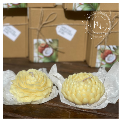 Duas velas florais amarelas sobre papel branco e madeira, caixas castanhas ao fundo