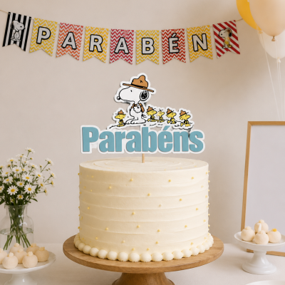 Bolo de aniversário branco com topper Parabéns e personagens Snoopy sobre base de madeira.