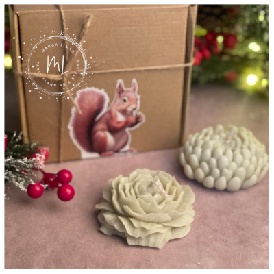 Duas velas decorativas brancas sobre superfície rosa com caixa e adesivo de esquilo ao fundo