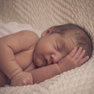Bebé recém-nascido adormecido sobre manta branca texturada