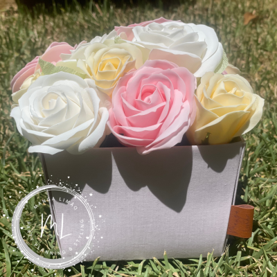 Arranjo de flores artificiais coloridas numa caixa cinzenta sobre relva com logótipo de marca