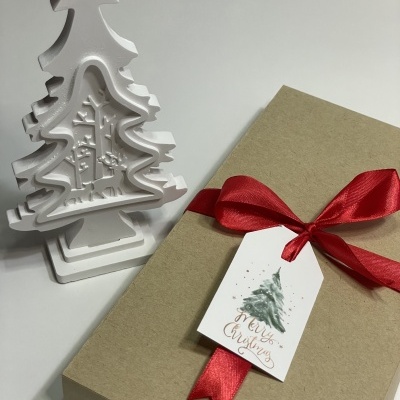 Árvore de Natal decorativa branca junto a caixa de presente com fita e etiqueta