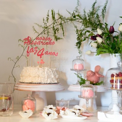 Bolo de casamento com decoração de chantilly e flores, doces variados e jarra de limonada numa mesa decorada
