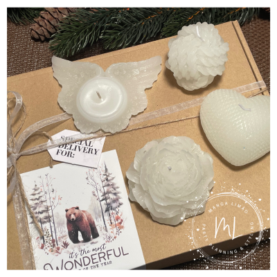 Conjunto de quatro velas brancas em formas variadas sobre caixa de papel castanho com laço e cartão decorativo