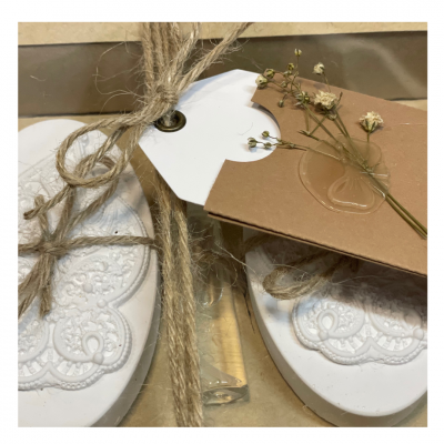 Sabonetes decorativos brancos com padrão floral em relevo, frasco de vidro e cartão com flores secas