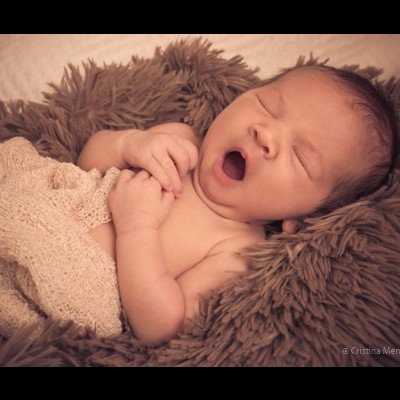 Bebé adormecido numa manta bege sobre uma superfície castanha felpuda