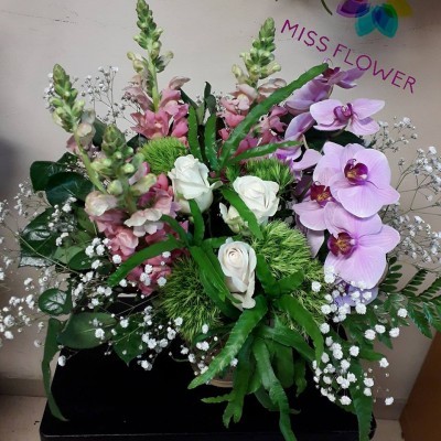 Arranjo floral com rosas brancas, orquídeas lilases e folhagem variada