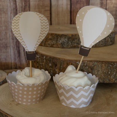 Dois cupcakes decorados com toppers de balões de ar quente em papel bege e branco sobre suportes de madeira