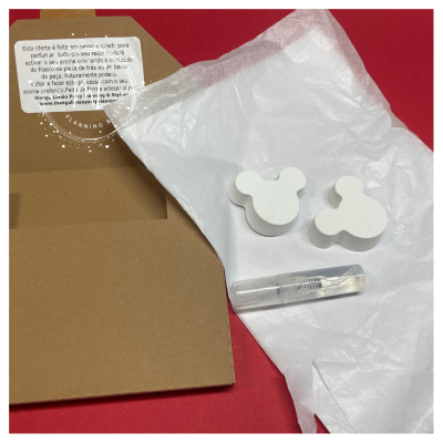 Difusores de aroma brancos em forma de cabeça de rato e frasco transparente em papel branco sobre fundo vermelho e embalagem castanha.