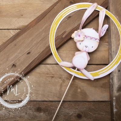 Topper circular amarelo e branco com coelho rosa decorativo numa parede de madeira