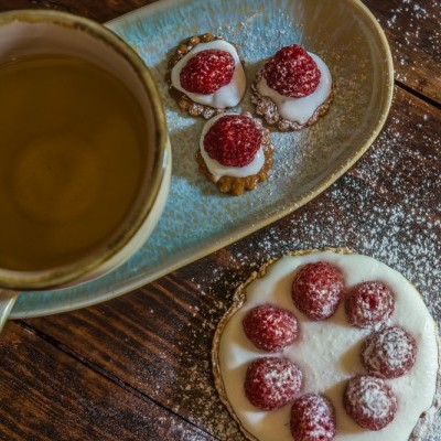 Chávena azul com chá verde e bolachas com framboesas sobre mesa de madeira