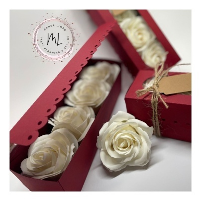 Caixas vermelhas com flores artificiais brancas em forma de rosa e etiqueta com cordão rústico.