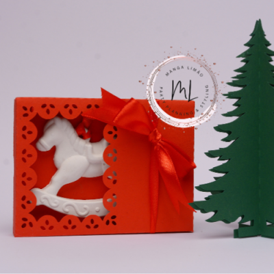 Caixa de presente laranja com cavalo de baloiço branco e fita laranja ao lado de uma árvore de Natal verde