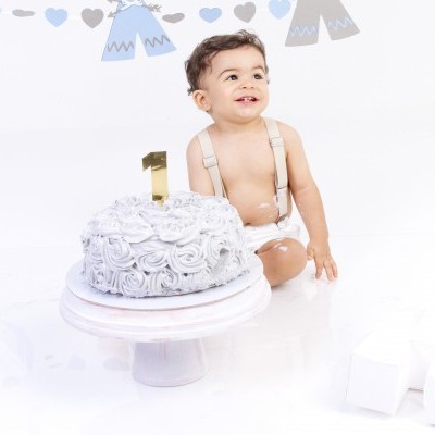 Criança com bolo do primeiro aniversário em fundo branco com decoração azul e branca.