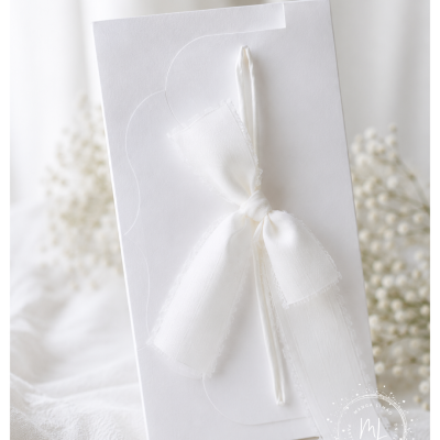 Convite branco com laço de tecido branco e fundo com flores desfocadas.