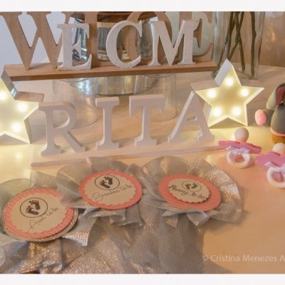 Decoração de mesa com letras de madeira, estrelas iluminadas, chupetas rosa, boneco elefante e medalhas para batizado.