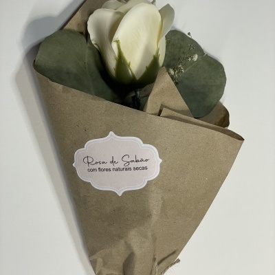 Ramo de rosa branca artificial com folhas verdes e flores naturais secas embrulhado em papel castanho