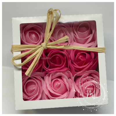 Caixa branca com nove velas rosas em forma de flor e laço de palha