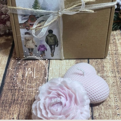 Caixa castanha com laço dourado, vela rosa em forma de flor e coração, etiqueta com figuras humanas e neve.