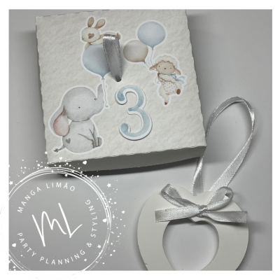 Caixa branca decorada com número 3 e animais, e anel branco com fita prateada