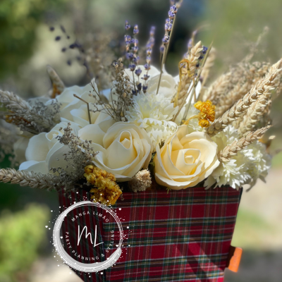 Arranjo floral artificial em suporte de tecido xadrez com flores creme e ramos secos