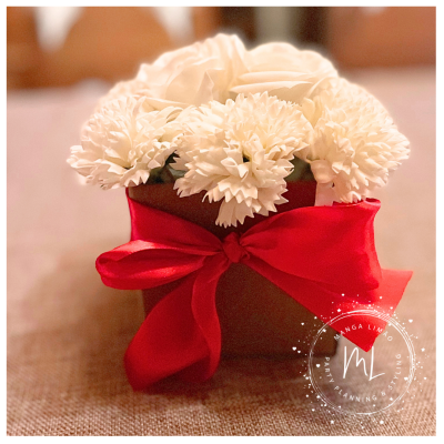 Arranjo floral com flores brancas em vaso castanho e laço vermelho.